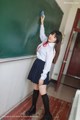 A woman in a school uniform standing in front of a blackboard.