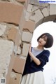 A woman leaning against a stone wall with her hand on her hip.