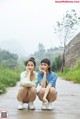 Two young women sitting on the side of a road.