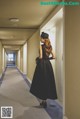 A woman in a long black dress is walking down a hallway.